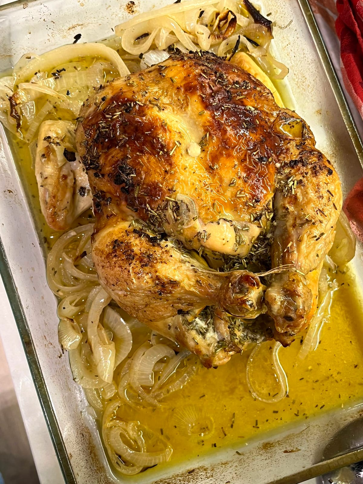 Whole roasted herb chicken on onions in a glass dish